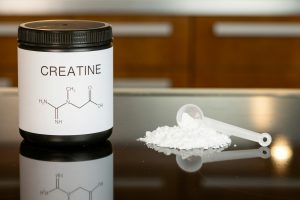 Pot de créatine en poudre et cuillère doseuse remplie de poudre blanche